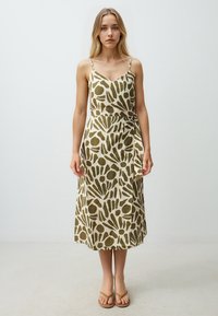 Beige wikkeljurk met groene abstracte patronen, voorzien van spaghettibanden en een gestrikte taille, gemaakt van lichte stof.