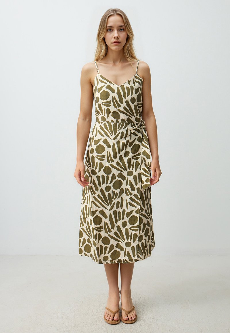 Beige wikkeljurk met groene abstracte patronen, voorzien van spaghettibanden en een gestrikte taille, gemaakt van lichte stof.