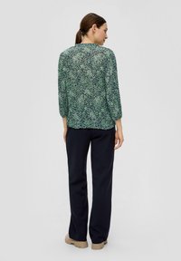Groene blouse met patroon en 3/4 mouwen, van lichtgewicht stof, ronde halslijn. Gepaard met donkerblauwe broek en beige schoenen. Eenvoudig ontwerp.