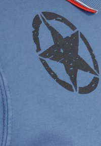 Bl å tyg t-shirt med en svart stjärndesign inom en cirkulär kontur. Har en kontrasterande röd krage och en slät textur.