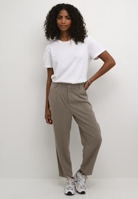 Witte korte mouwen t-shirt, lichtbeige hoge taille broeken met plooien aan de voorkant, en grijze sneakers met reflecterende accenten.