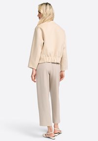 Giacca beige cropped con vita elasticizzata, maniche lunghe e design semplice, abbinata a pantaloni ampi beige chiaro e sandali.