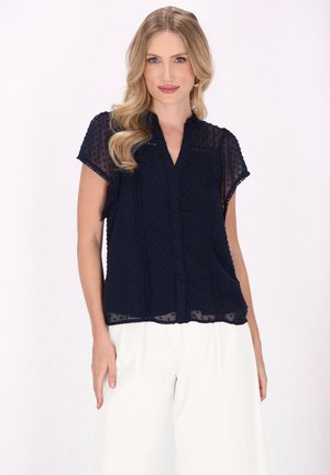 Blouse bleu marine en tissu léger avec des manches courtes, des pois subtils, un devant boutonné et une coupe décontractée.