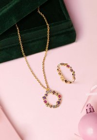 Collar de tono dorado con un colgante circular que presenta piedras de varios colores. Un anillo a juego en tono dorado con un diseño similar de piedras.