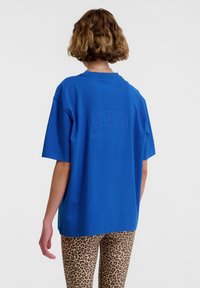 Blå bomullströja med en avslappnad passform och korta ärmar. Har en präglad logotyp på ryggen. Kombineras med leopardmönstrade byxor.