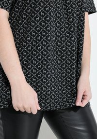 Černé tričko s krátkým rukávem s diamantovým vzorem, které obsahuje šedé motivy jelenů, kombinované s černými lesklými legínami. Hladký povrch po celém oblečení.