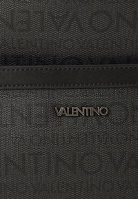 Sac en matériau texturé noir avec un accent en cuir lisse. Présente un logo métallique "VALENTINO" sur le devant.