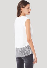 Top blanco sin mangas con un diseño de malla, con un back sólido blanco y acentos negros. El tejido parece ligero y texturizado.