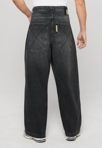 Jeans neri a gamba larga con una texture sbiadita, dotati di due tasche posteriori e un'etichetta del marchio sulla vita. Aperture della gamba svasate.