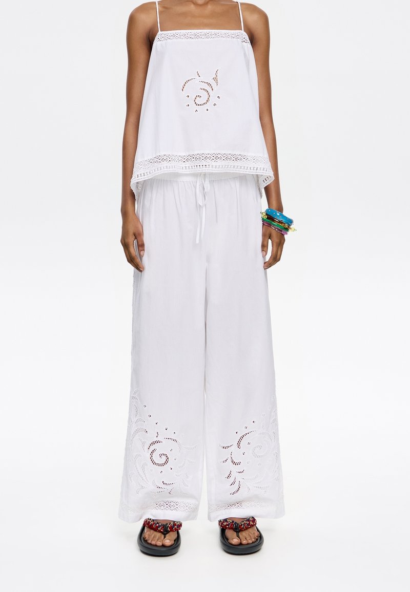 Witte katoenen tweedelige outfit bestaande uit een cropped tanktop met kantafwerking en palazzo pants met uitgesneden bloemenborduurwerk aan de zoom.