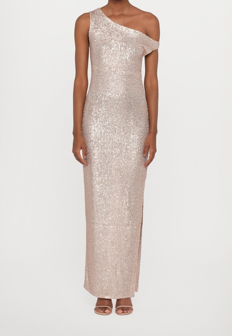 Femme portant une robe longue jusqu'au sol, asymétrique à une épaule, rose clair à sequins avec une fente, associée à des talons ouverts couleur nude.