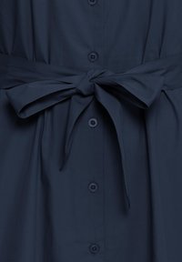 Vêtement bleu foncé à boutons avec ceinture en tissu nouée en un nœud à la taille.