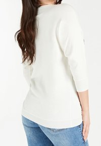 Maglione bianco a maglia con maniche a tre quarti, polsini e bordo a coste, abbinato a jeans blu in denim. Tessuto morbido, vestibilità casual.