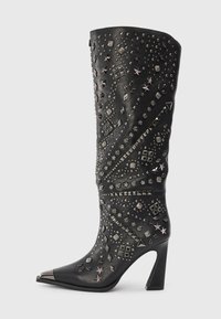 Bota de cuero negro de tacón alto con punta metálica puntiaguda y adornos plateados decorativos con tachuelas y embellishments en forma de estrella a lo largo del caña y del pie.