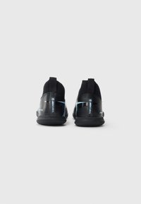 Une paire de chaussures de sport Nike Mercurial noires montrées de l'arrière sur un fond blanc uni.