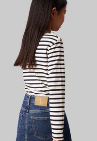 Maglietta a maniche lunghe a righe in crema e nero, abbinata a jeans in denim blu a vita alta con etichetta in pelle Calvin Klein sul retro.