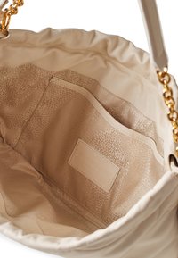 Beiger Lederhandtaschen Innenraum mit weicher Textur; verfügt über ein glattes Futter und eine separate Tasche, sichtbares geprägtes Logoschild. Goldene Kettenakzente oben.