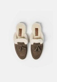 Zapatillas de ante marrón con un forro de piel blanca, que presentan un detalle de borlas y una etiqueta de cuero, con punta redondeada y diseño slip-on.