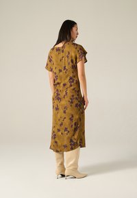 Braunes Blumenkleid aus weichem Stoff, mit kurzen Ärmeln, lockerem Schnitt und mittellanger Länge, kombiniert mit beigen kniehohen Stiefeln.