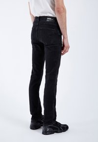 Jeans de denim negro con un diseño ajustado, estilo de cinco bolsillos y cintura de altura media, vistos desde atrás, con una cinturilla de marca y una textura suave.