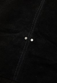 Black suede fabric with a soft texture, featuring two metallic studs and contrasting stitching along the seam.