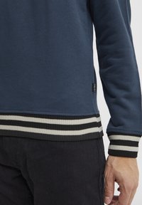 Navyblauwe sweatshirt met geribbelde zwarte en witte gestreepte manchetten en onderrand. Zachte textuur met een label aan de zijkant.