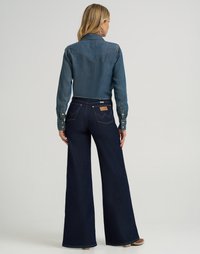 Jeansskjorta med mörkblå tvätt, västerländsk yoke-design, knappstängning fram och långa ärmar, tillsammans med högmidjade, vida mörka jeans.