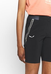 Černé sportovní šortky s kapsami na zip, texturovaným pasem a reflexními doplňky. Mají těsný střih a hladkou, lehkou tkaninu.