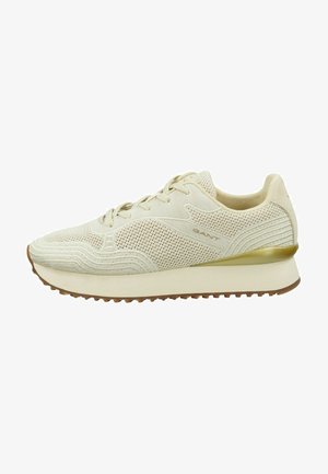 Beige athletic shoe with mesh and textured detailing, round toe, laces, and a light outsole. Features a subtle gold accent on the heel.
