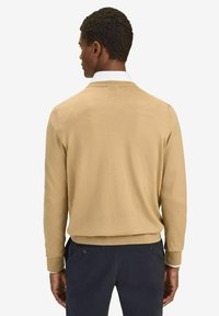 Vaaleanbeige neulepusero, jossa on pyöreä kaula-aukko, resorit hihansuissa ja helma. Tyylitelty valkoisen kauluspaidan päälle, esitelty takaa.