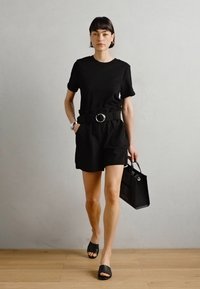 Haut noir à manches courtes associé à un short noir taille haute, orné d'une ceinture avec une boucle ronde. Accessoirisé avec un petit sac à main noir et des sandales à enfiler.