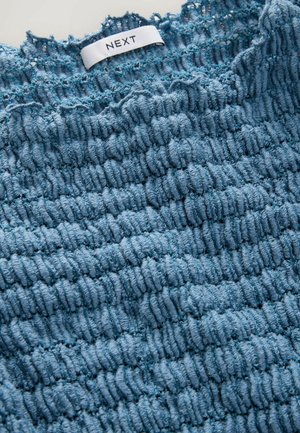 Vêtement bleu texturé avec un motif côtelé. Fabriqué en tissu doux, avec une étiquette portant la mention "NEXT" au niveau du col.