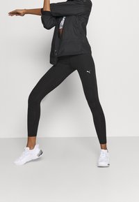 Svarta träningsleggings med en åtsittande design och texturerad paneling, kombinerade med en svart jacka och vita sneakers med silveraccenter.