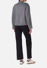 Veste gris en mélange de laine avec un col arrondi, coupe décontractée et manches longues, associée à un pantalon noir à jambe droite et des baskets blanches.