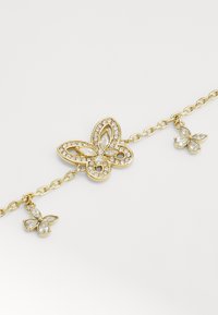 Gouden armband met een vlinderbedel en heldere strassstenen. Twee kleinere vlinderbedels hangen van een gekoppelde ketting.