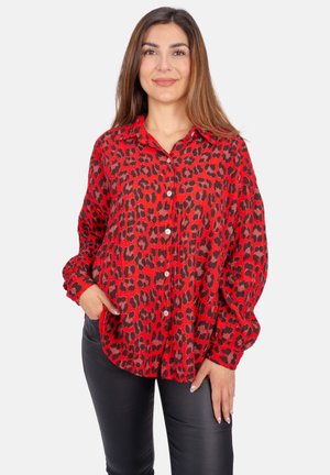 Chemise à imprimé léopard rouge avec un devant à boutons, coupe décontractée et manches longues, fabriquée en tissu léger. Associée à un pantalon noir.