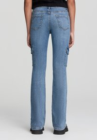 Jasnoniebieskie dżinsy o rozkloszowanym kroju, z dwoma bocznymi kieszeniami cargo i dwiema tylnymi kieszeniami, widocznym przeszyciem oraz średnim stanem.