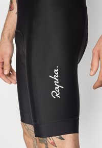 Černé cyklistické kraťasy vyrobené z hladké, pružné látky. Obsahují bílé logo "Rapha", mají přiléhavý střih a ploché švy pro pohodlí.