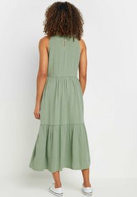 Grön, ärmlös kl änning med en lager-på-lager kjol, tillverkad av mjukt tyg. Har en knappstängning i ryggen och en flowy design.