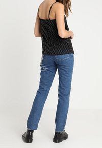 Černý top s puntíky na tenkých ramínkách, spárovaný s volně střiženými světle modrými džínami s trhlinami a roztrženými okraji. Černé kotníkové boty.