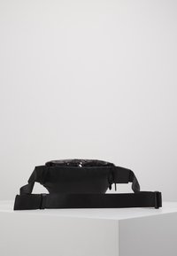 Marsupio nero con frontale in paillettes, caratterizzato da una superficie testurizzata, design piatto, tracolla regolabile e una chiusura a zip discreta.