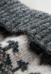 Woolen fabric in dark gray with a textured ribbed pattern, layered over a lighter fabric featuring a black and beige geometric design.