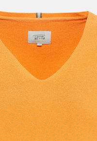 Pomarańczowy sweter z dekoltem w kształcie litery V, z teksturowanym splotem. Widoczna metka z logo marki "camel active" na białym tle.