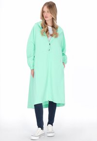 Világoszöld, könnyű esőkabát kapucnival, elülső cipzárral és rugalmas szegélyekkel. Oldalzsebekkel és középhosszúságú kialakítással.