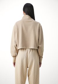 Korte beige sweatshirt met een hoge kraag en lange mouwen, gecombineerd met beige gemusterde broeken met een herhaald logo ontwerp.
