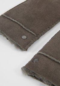 Tissu en feutre marron avec des coutures visibles et une doublure interne douce ; présente de petits boutons en métal pour la fermeture ; forme rectangulaire.