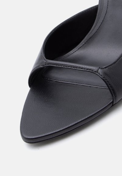 Μαύρο δερμάτινο mules σανδάλι με ανοιχτά δάχτυλα, τετράγωνη μύτη και μία φαρδιά λουρίδα μπροστά.