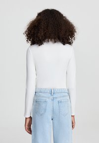 Maglietta bianca a maniche lunghe con silhoutte aderente, abbinata a jeans alta vita di colore azzurro chiaro con tasche posteriori e vestibilità morbida.