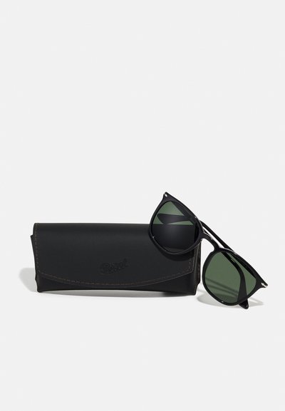 Black sunglasses with green lenses, featuring a sleek design and prominent temple accents, paired with a black leather case.