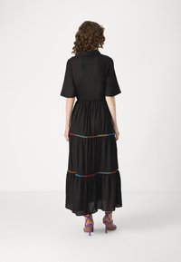 Rochie maxi neagră cu mâneci scurte, având un detaliu colorat de cusătură la talie. Modelul poartă sandale cu toc înalt de culoare mov.